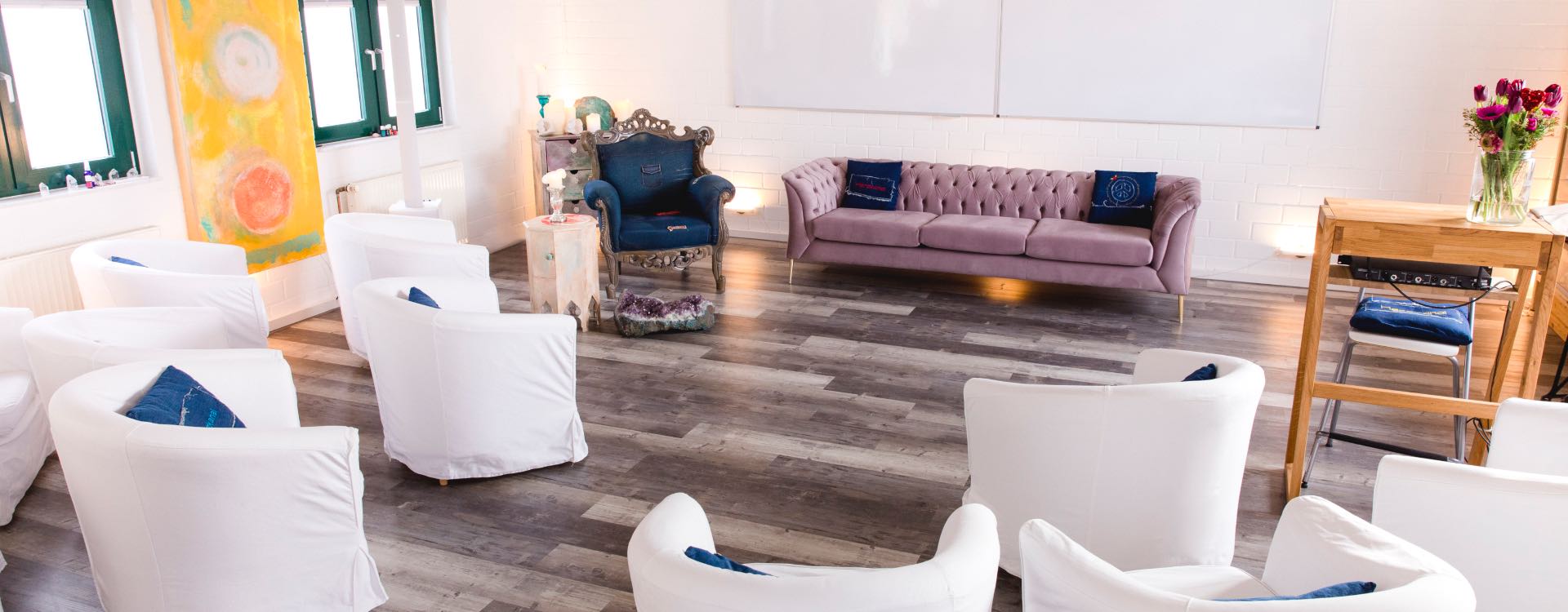 Heller Herzkanal-Seminarraum mit weißen Sesseln im Kreis, rosa Sofa und Kristallen